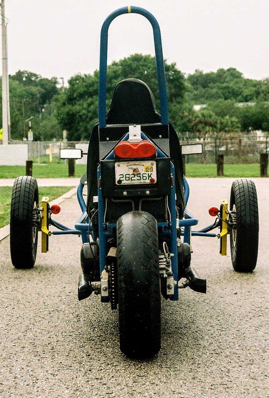 The rear view of the second Tampa Trike prototype showcases its sleek design, with a sturdy frame and robust tires that exude stability and control on the road. Judging by the rear tire, testing is biased toward left-hand turns. Perhaps from extensive oval track testing? US patents 11,753,105 and 11,279,430.